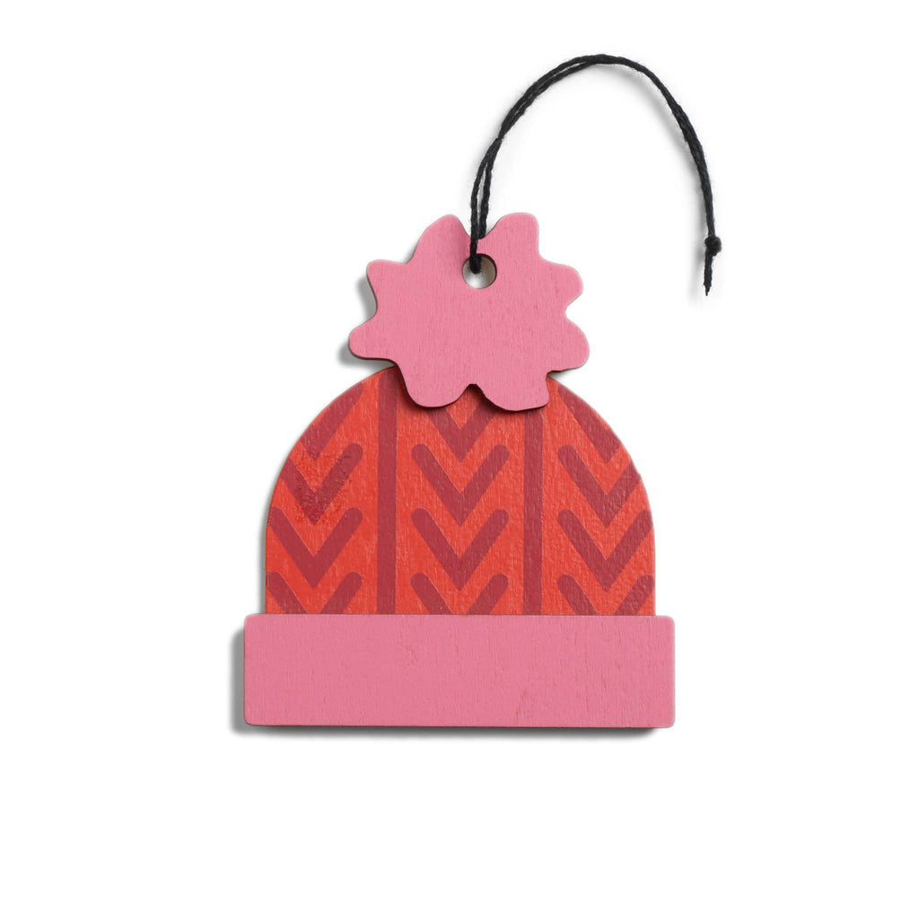Colorful beanie-shaped wood ornament with pink brim and pompom and red pattern on a white background.