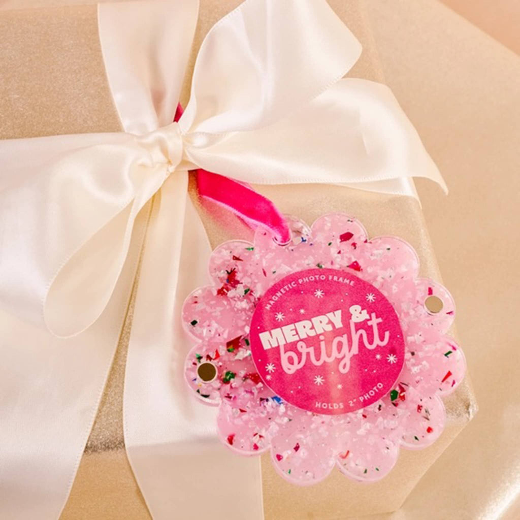 Confetti pink acrylic round magnetic photo frame with scalloped edge and a red ribbon loop on a packaged gift.