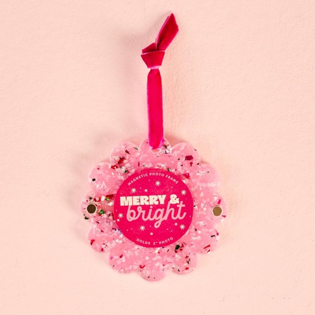Confetti pink acrylic round magnetic photo frame with scalloped edge and a red ribbon loop on a pink background.