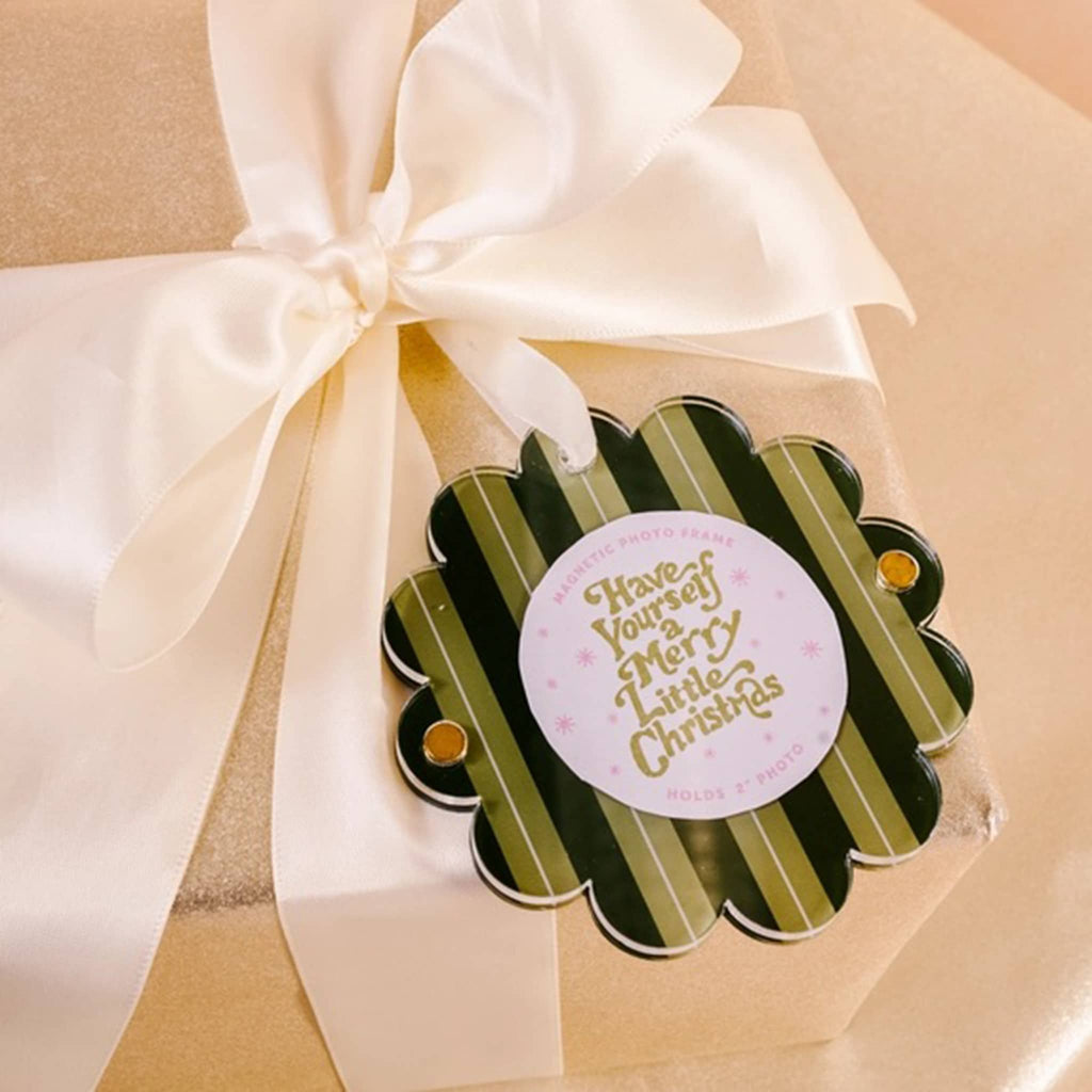 Green striped acrylic round magnetic photo frame with scalloped edge and a white ribbon loop on a gift wrapped box.