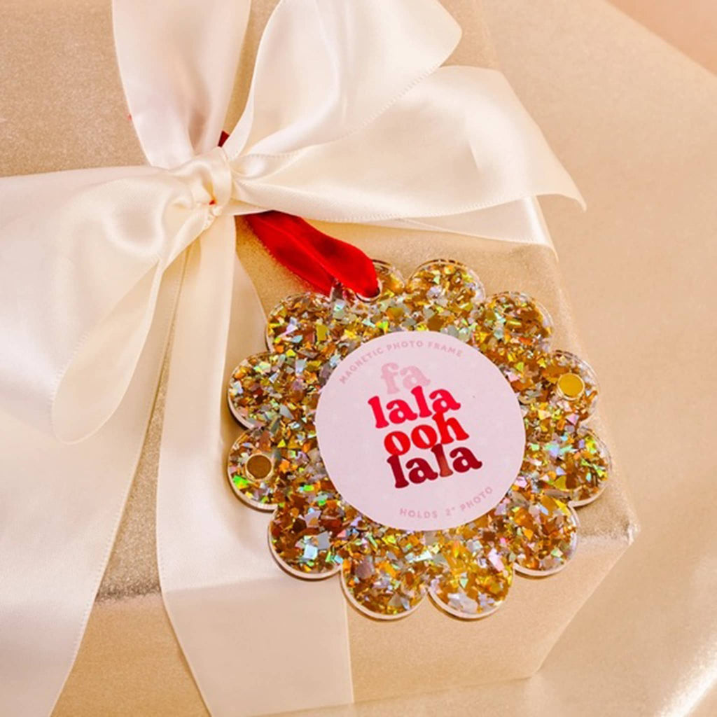 Gold glitter round acrylic magnetic photo frame with scalloped edge and a red ribbon loop on a wrapped gift box.