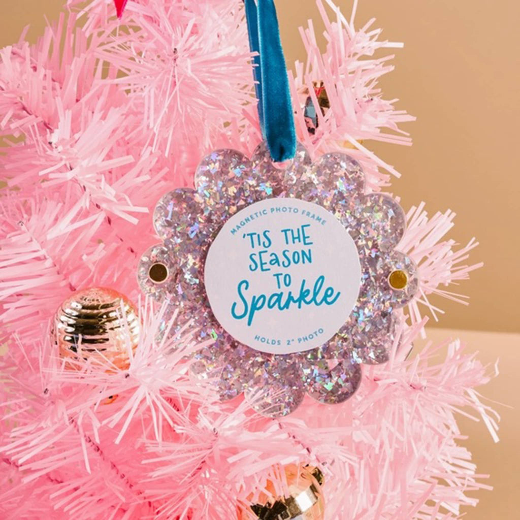 Silver glitter round acrylic magnetic photo frame with scalloped edge and a blue ribbon loop on a pink Christmas tree.
