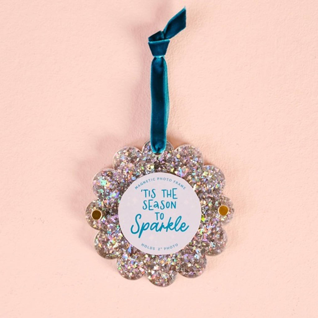 Silver glitter round acrylic magnetic photo frame with scalloped edge and a blue ribbon loop on a pink background.