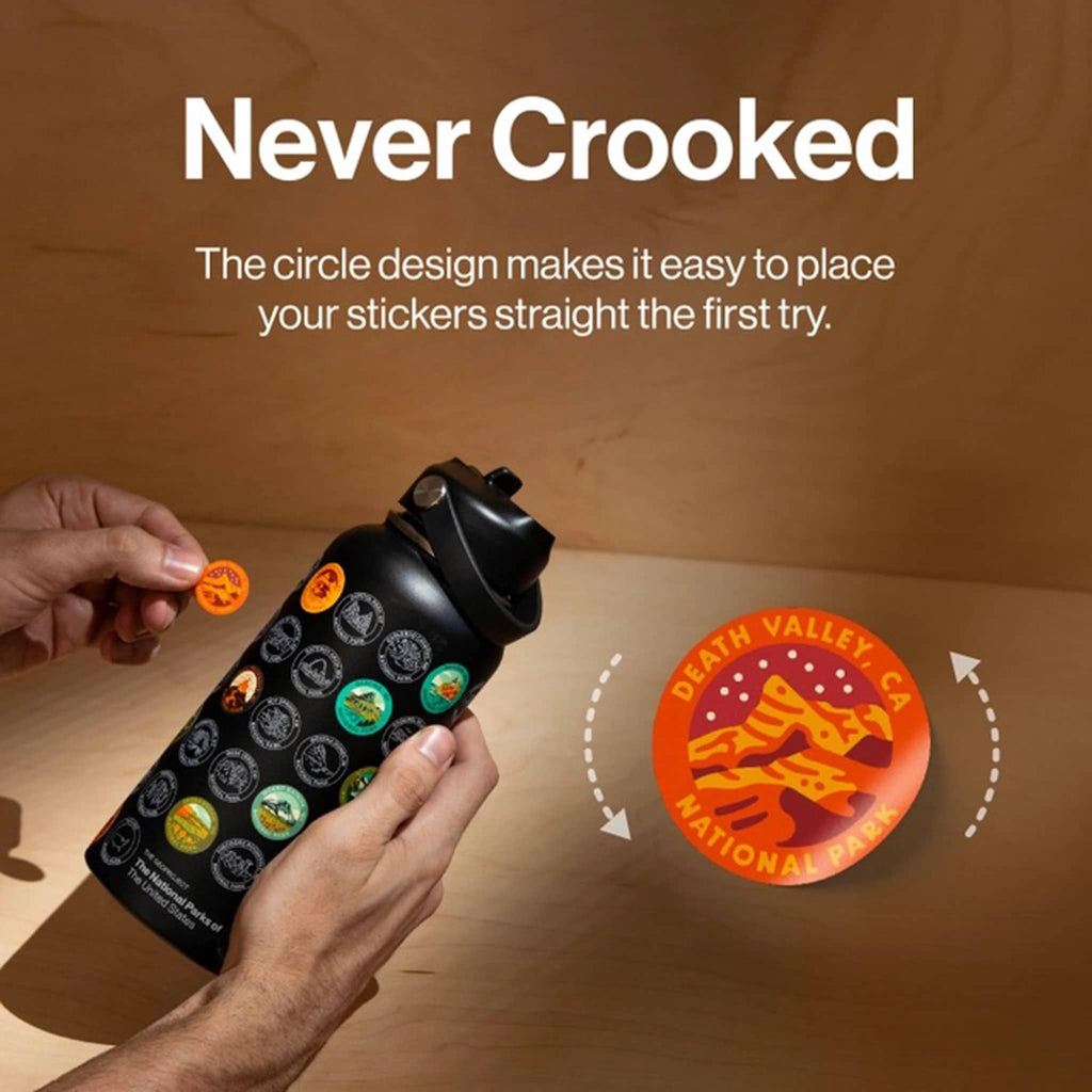 Person holding a black bottle with stickers, featuring 'Never Crooked' text and a logo.