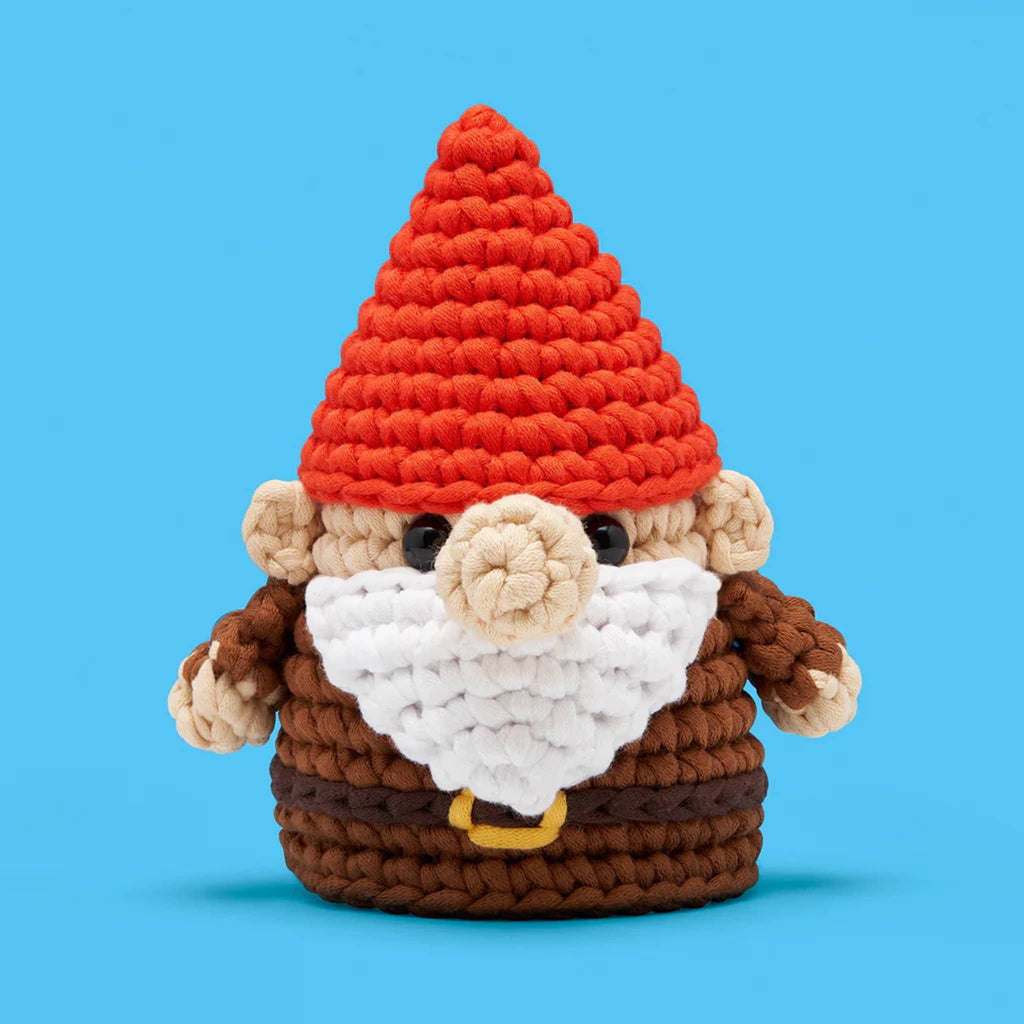 Crocheted gnome toy with a red hat on a blue background.