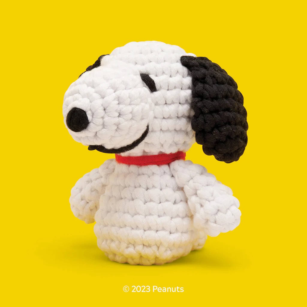 Crocheted white dog toy with black ears and red collar on a yellow background, featuring Peanuts branding.