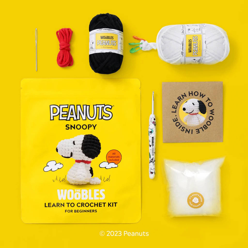Packaging and contents of The Woobles Snoopy beginner crochet kit on yellow background.