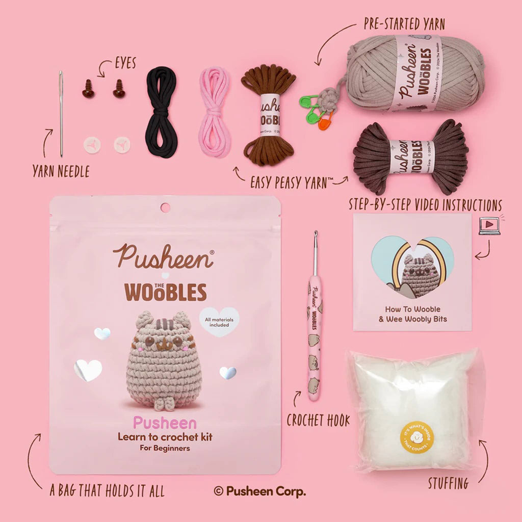 Packaging and contents of The Woobles Pusheen crochet kit on a pink background.
