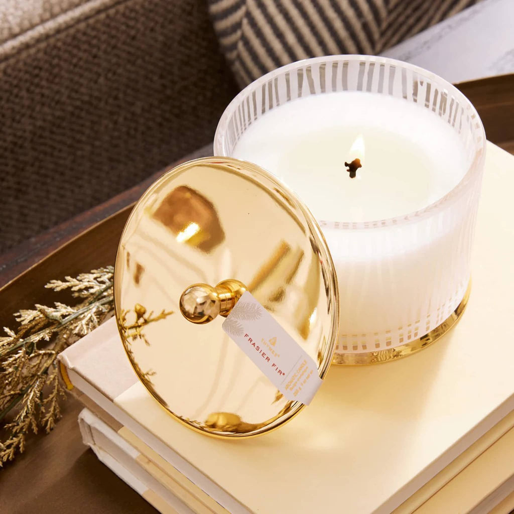 White candle with gold lid on a wooden surface.