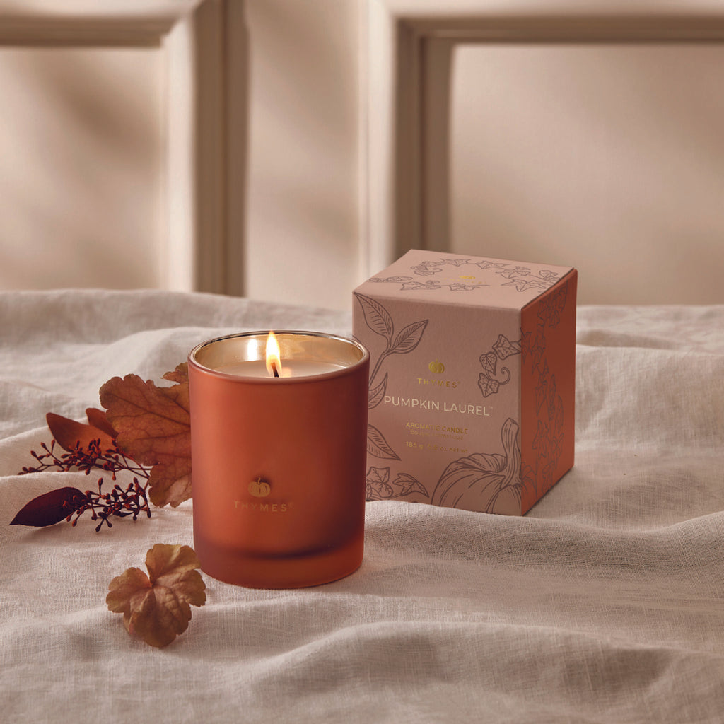 Thymes 6.5 ounce Pumpkin Laurel scented votive candle in burnt orange frosted mercury glass vessel with box, wick is lit.