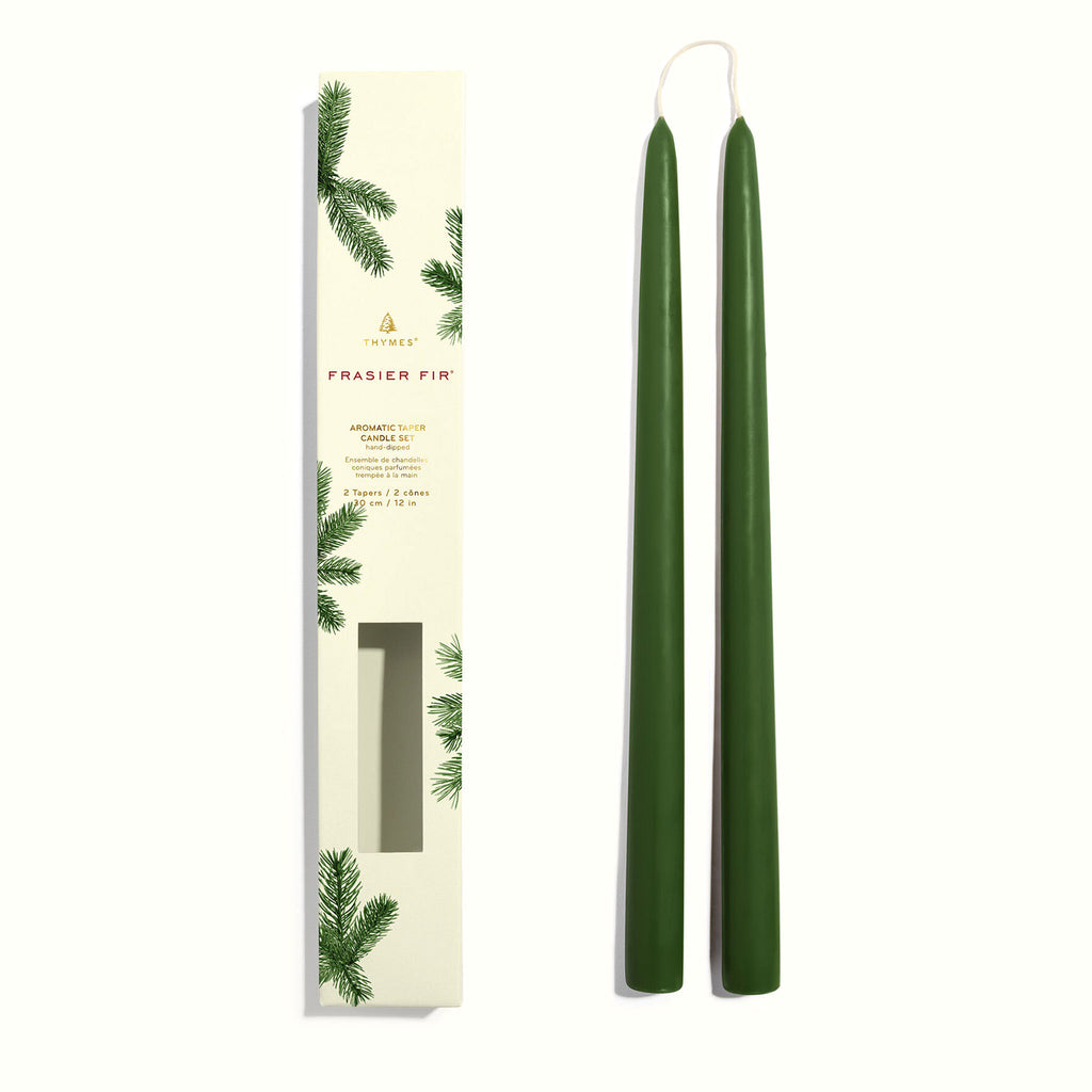 Thymes Frasier Fir 12 inch aromatic taper candle set, 2 hand-dipped green wax candles with connecting cotton wick beside box packaging decorated with a pine needle design.