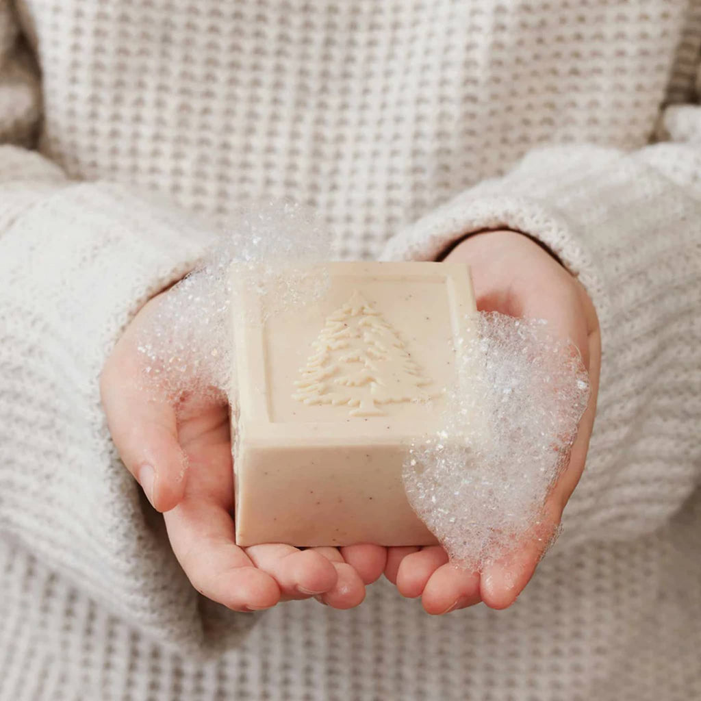 Person holding a bar of soap with a tree design in soapy water.