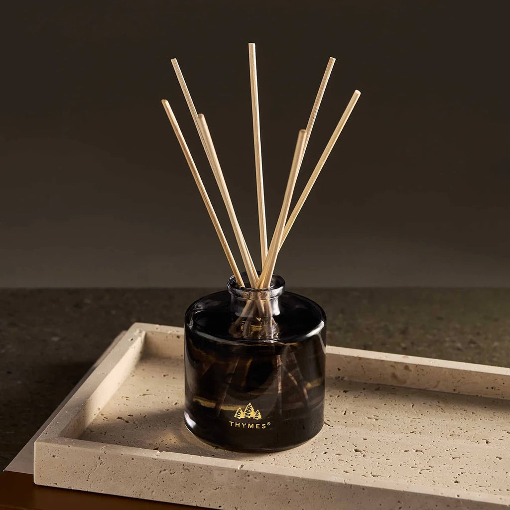 Black and white marbled glass diffuser with wooden reeds, on a stone surface.