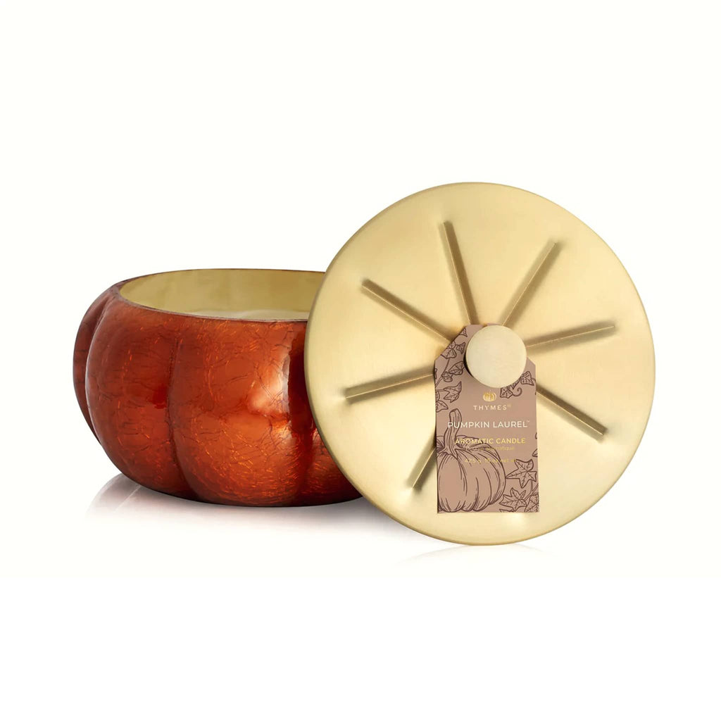 Pumpkin Laurel scented candle in decorative pumpkin-shaped container with a gold lid sitting in front, on a white background.