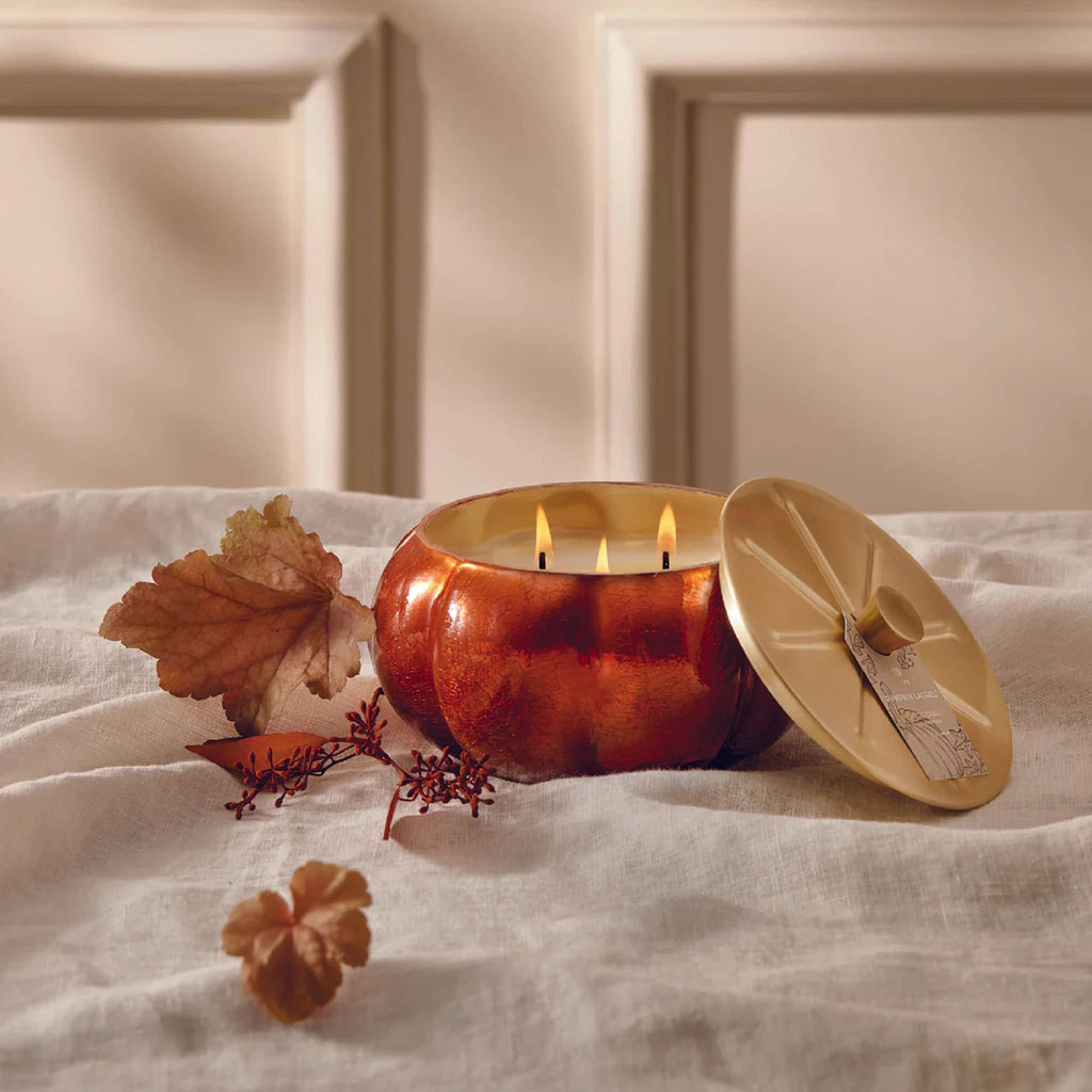Candle in a pumpkin-shaped holder with a lid on a textured surface.