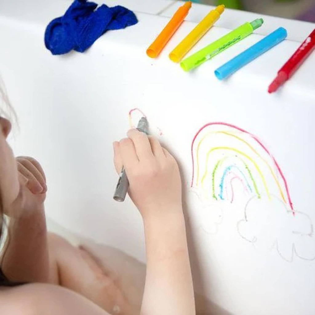 Child drawing a rainbow with bath crayons on the side of a bathtub.