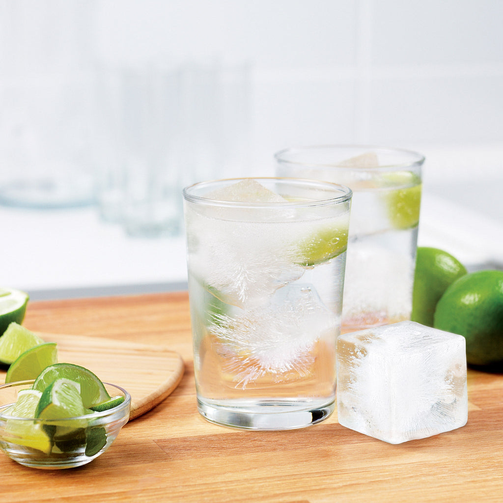 2 glasses with clear liquid and sliced limes with square ice cubes made with the Tovolo King Cube Ice Tray.