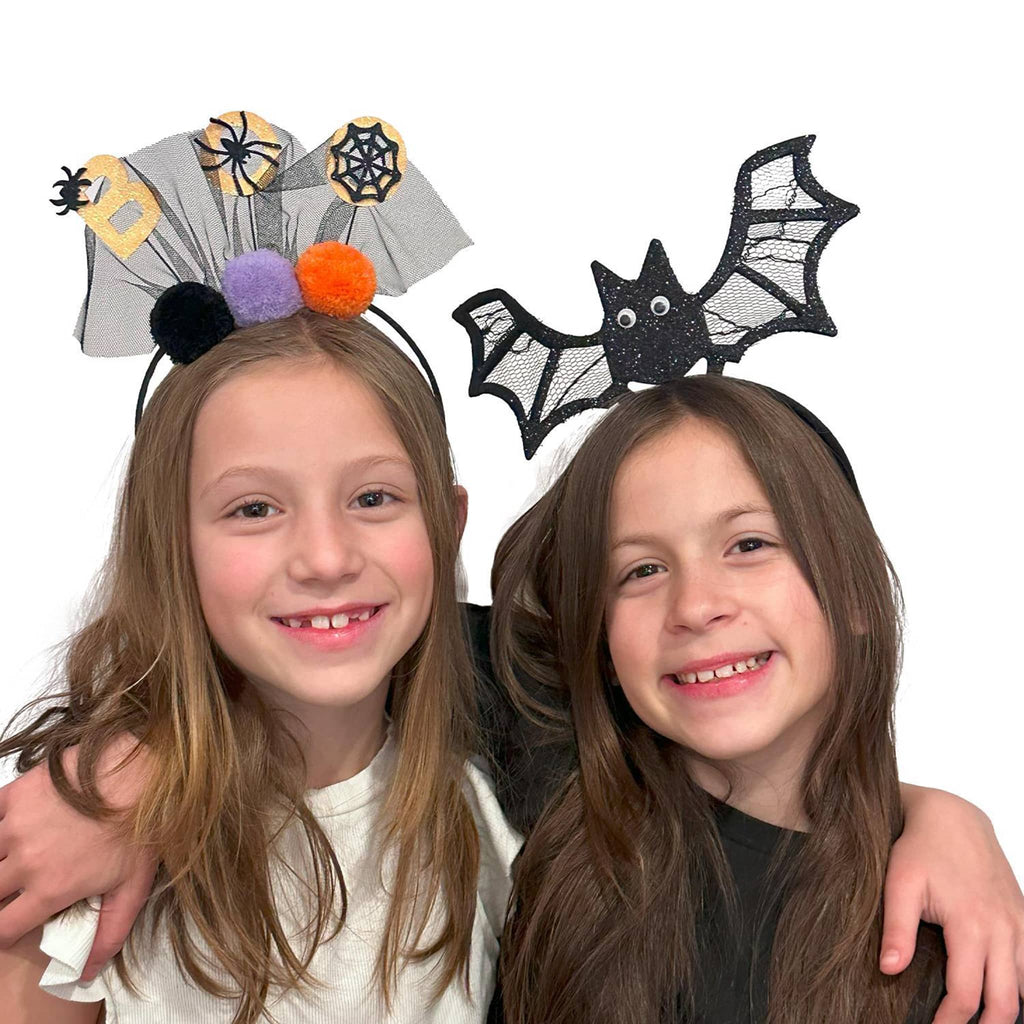 Two children wearing Halloween-themed headbands with spider webs, bats, and pom-poms on a white background.