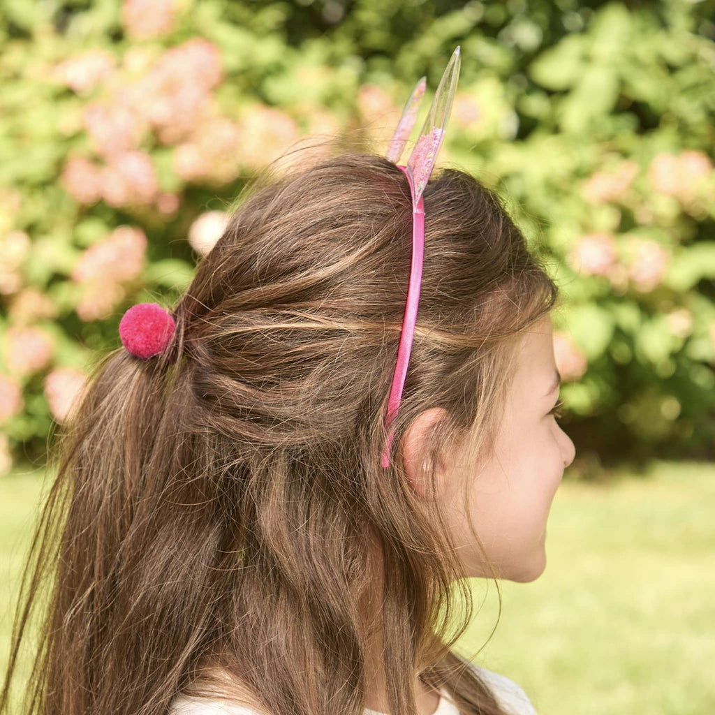 Two's Company Sequin Filled Bunny Ears Headband with Pompom Hair Tie in pink on a child.