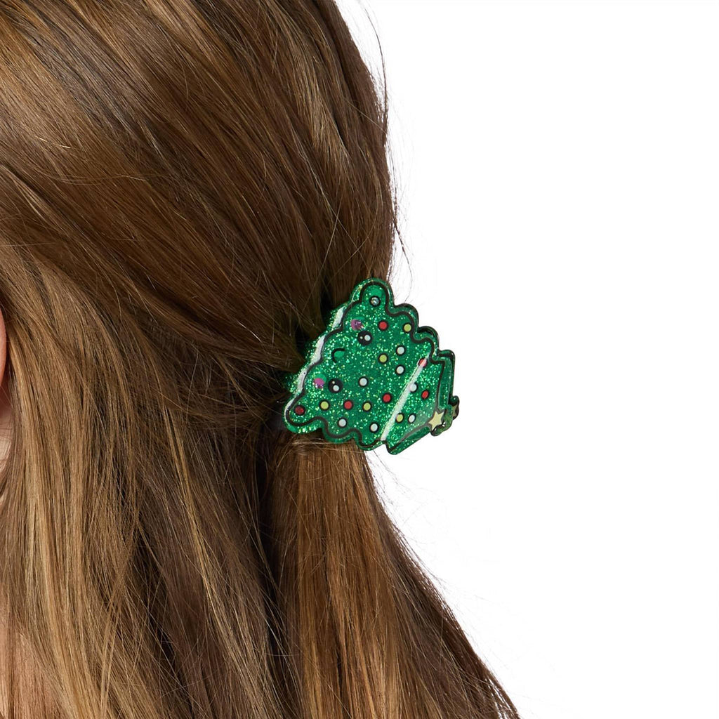 Decorative hair claw clip with a Christmas tree design on a person's ponytail against a white background.