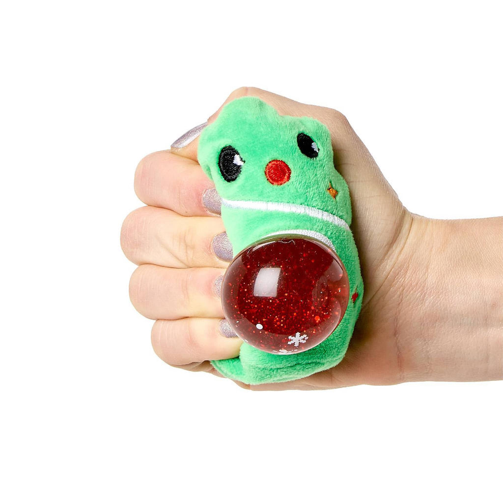 Hand holding a green plush toy with a red glitter ball inside, on a white background.
