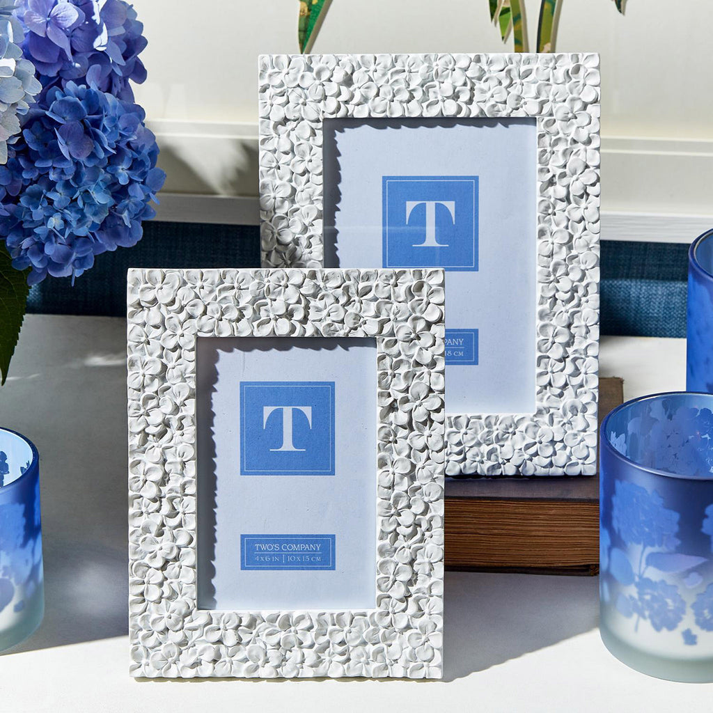 Two's Company 4x6 and 5x7 inch picture frames with white resin hydrangea pattern, front view, lifestyle shot with flowers, hydrangea pattern glasses and a book.