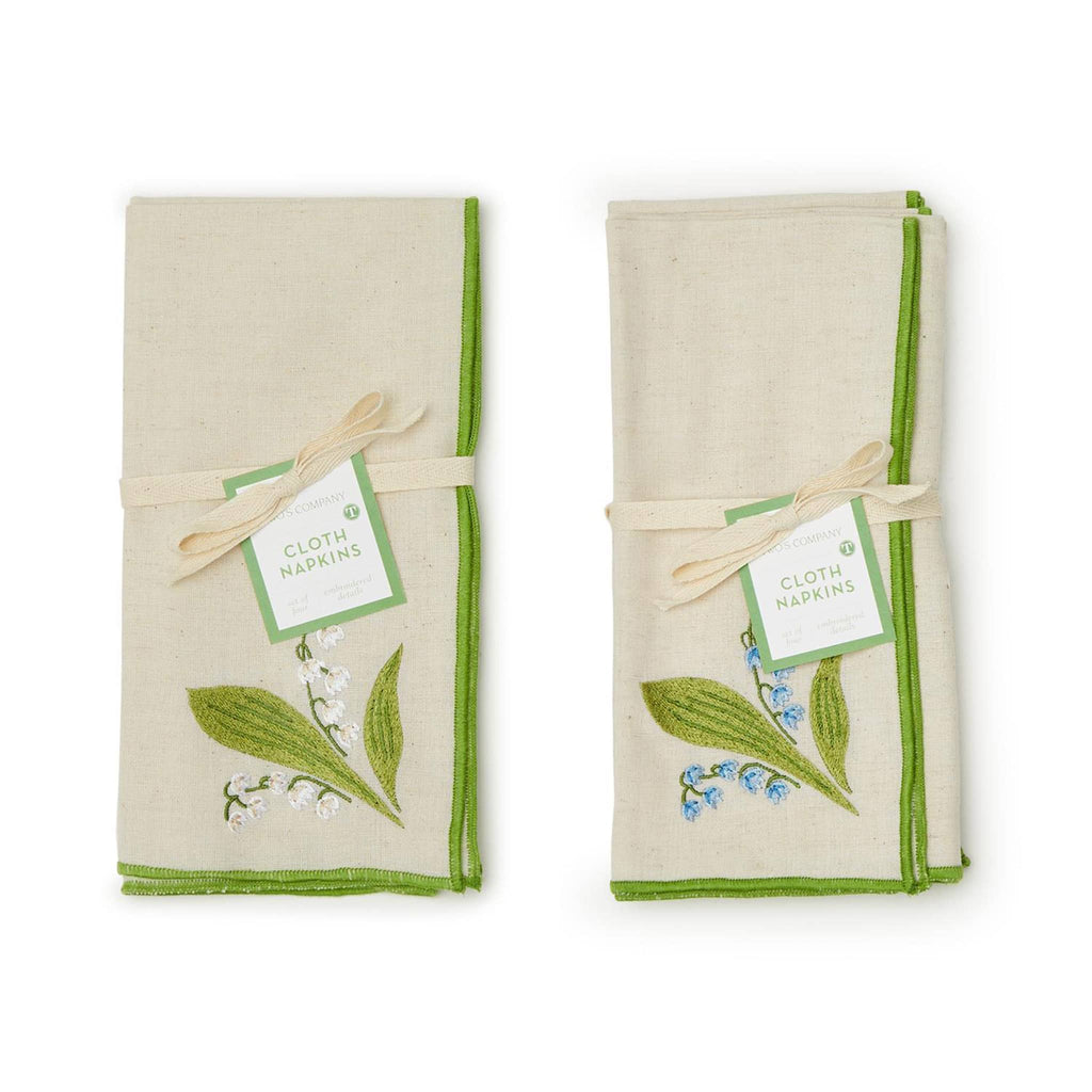 Two's Company Lily of the Valley embroidered cotton chambray napkins with white or blue flowers and green border, folded and tied with ribbon and tag.