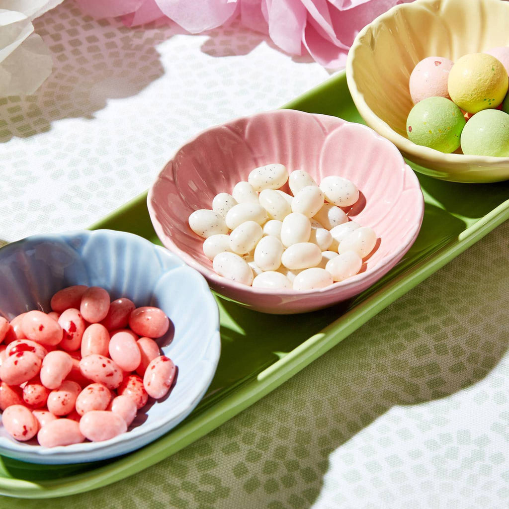 Two's Company pink, blue and yellow ceramic bowls that look like flowers with a green ceramic tray, filled with jelly beans and easter malted milk balls.