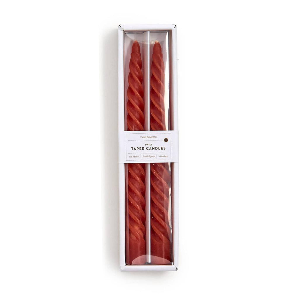 Two rust red taper candles in a white box on a white background.