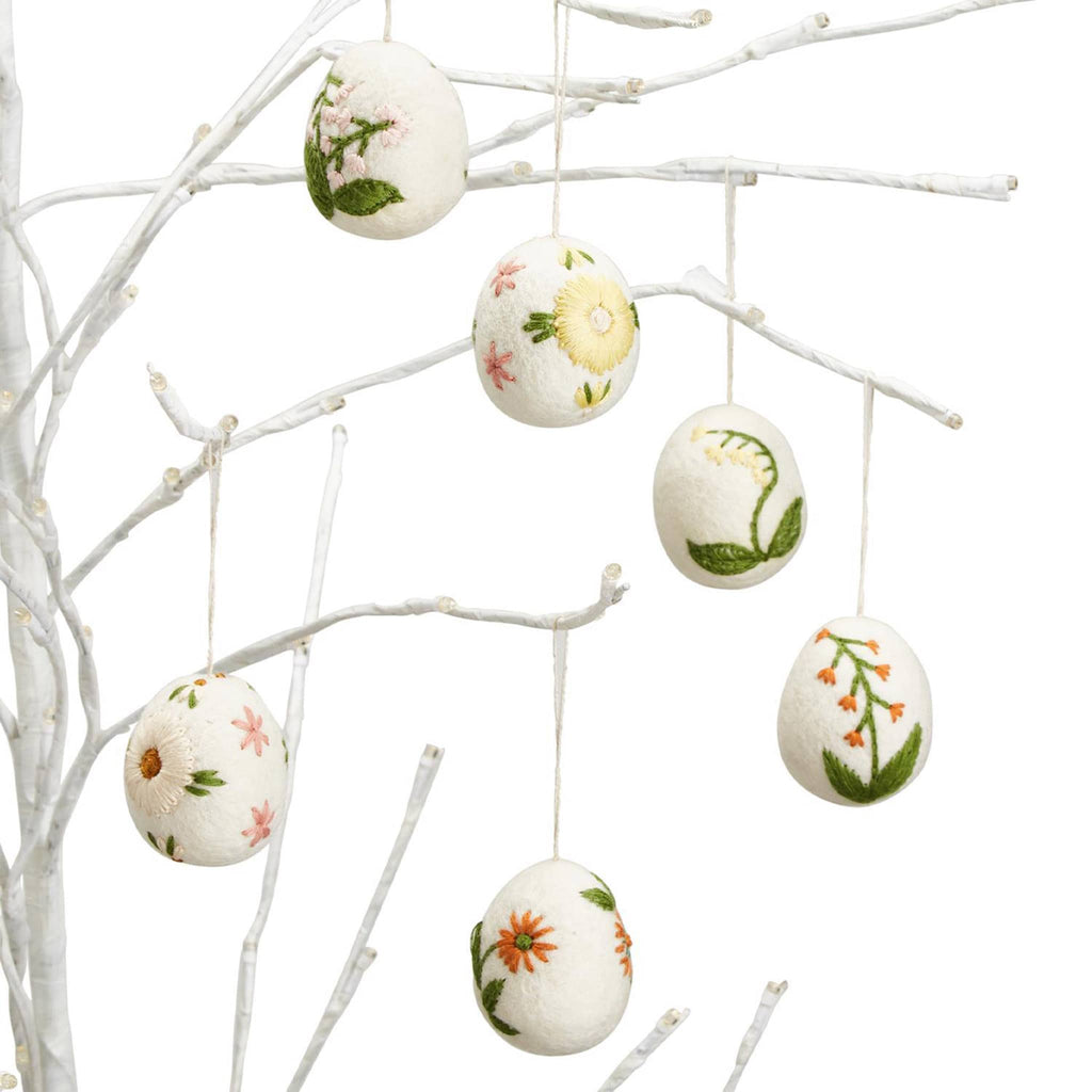 Two's Company wool felt eggs with colorful floral hand-embroidery in 6 designs with string, hanging on white branches.