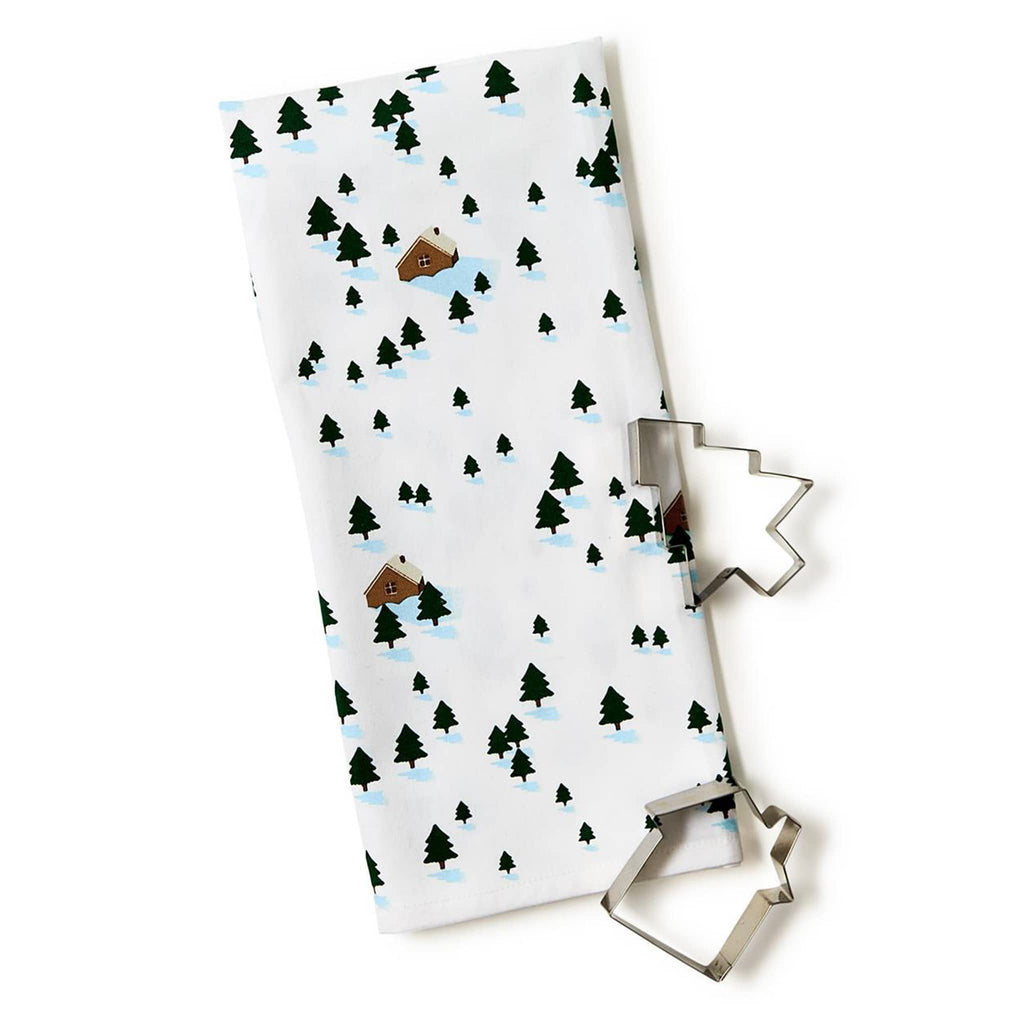 Two's Company winter scene dish towel folded with a tree and a house shaped cookie cutter.