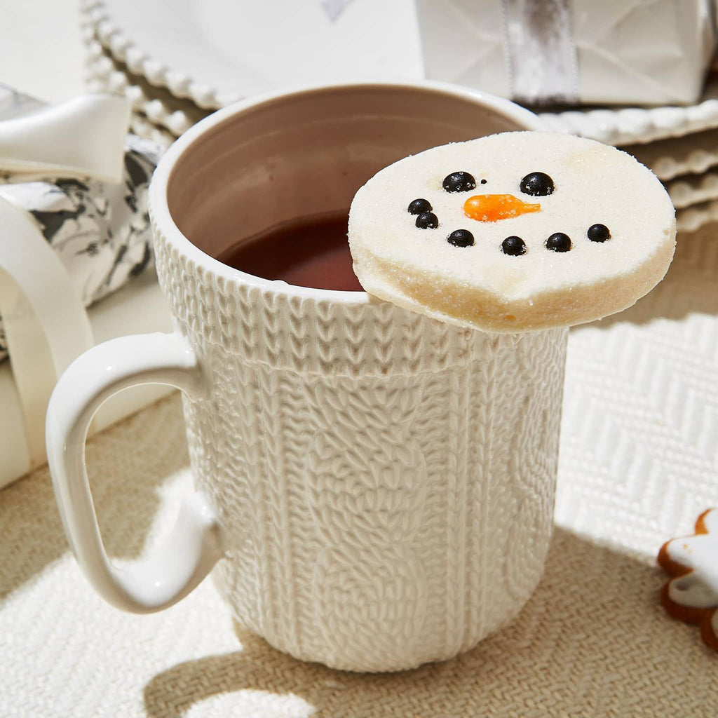 Two's Company white cable knit stoneware mug with vanilla flavored marshmallow hot cocoa topper resting on top of filled mug.