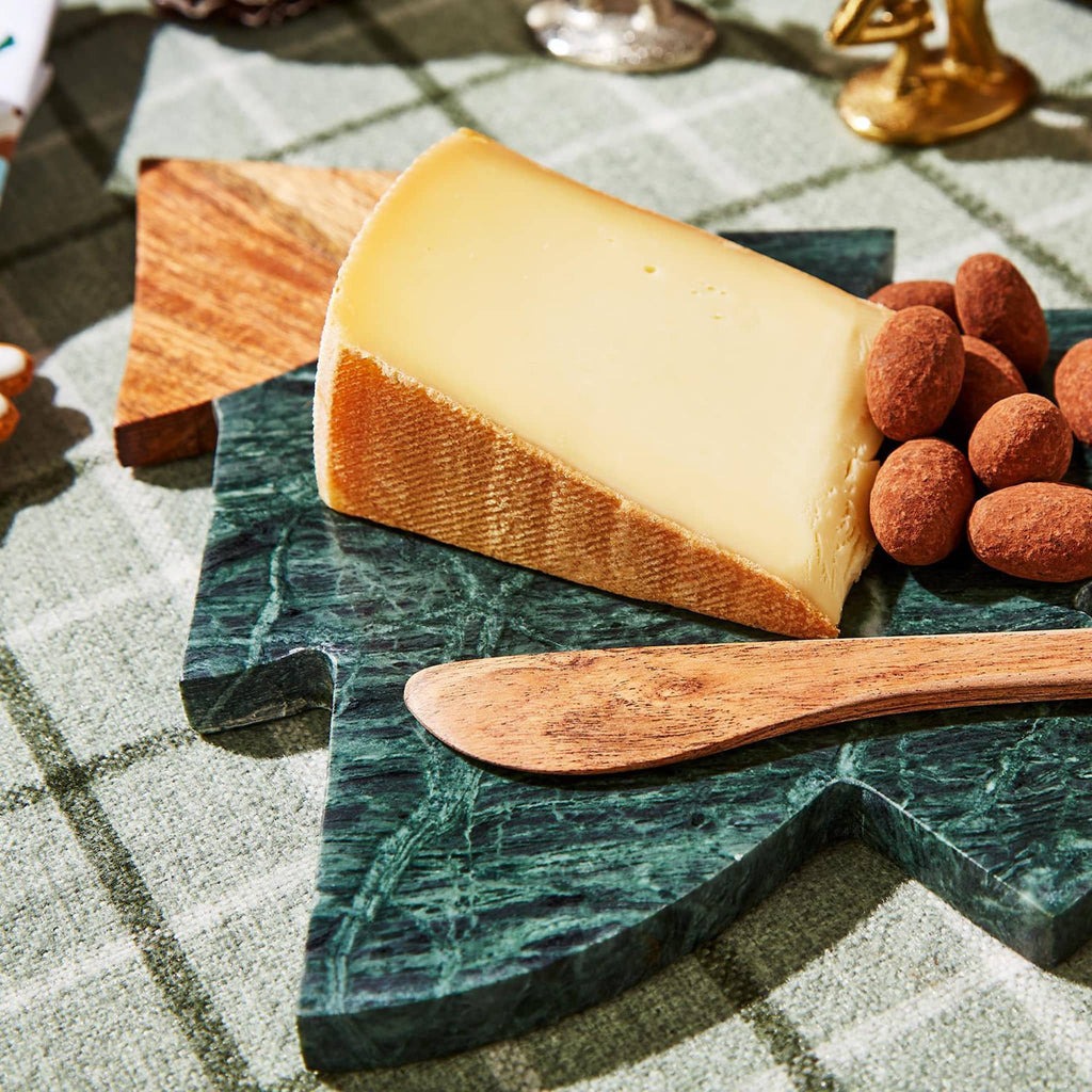 Two's Company green marble tree-shaped serving board with wood top and attached wood spreader, shown with cheese and nuts on top.