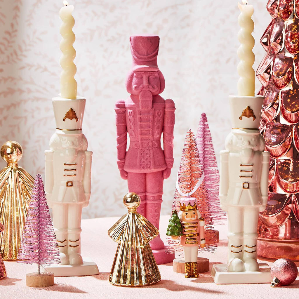 Two's Company Flocked Nutcracker figurine holiday decor in petal pink with other holiday figurines on a tablescape.