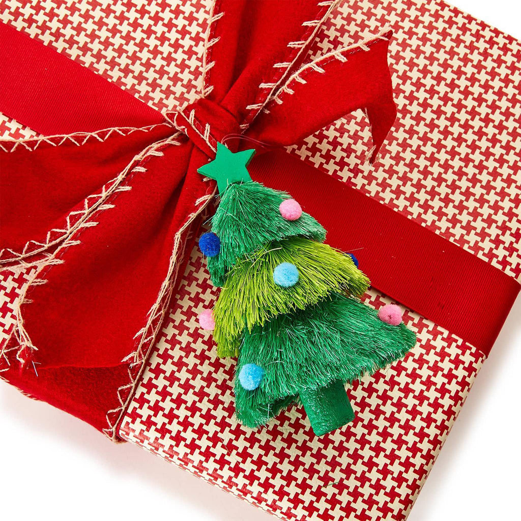 Two's Company decked out green natural fiber christmas tree with pompom ornaments on a wrapped gift as embellishment.