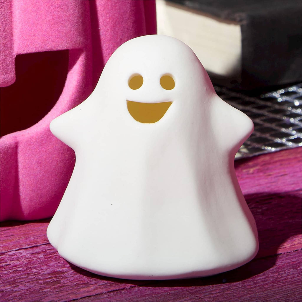 White ceramic ghost figurine with a smiling face on a pink surface with flocked pink pumpkin behind.