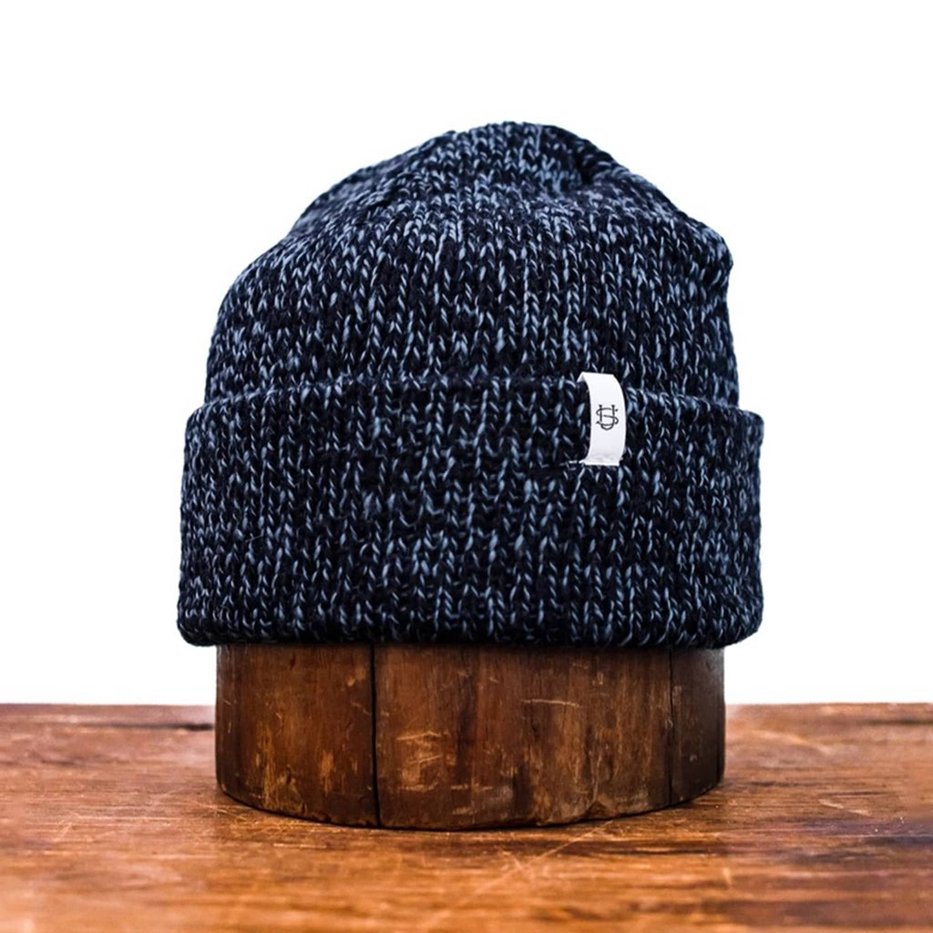 Blue and black knit wool beanie on a wooden block with a white background.