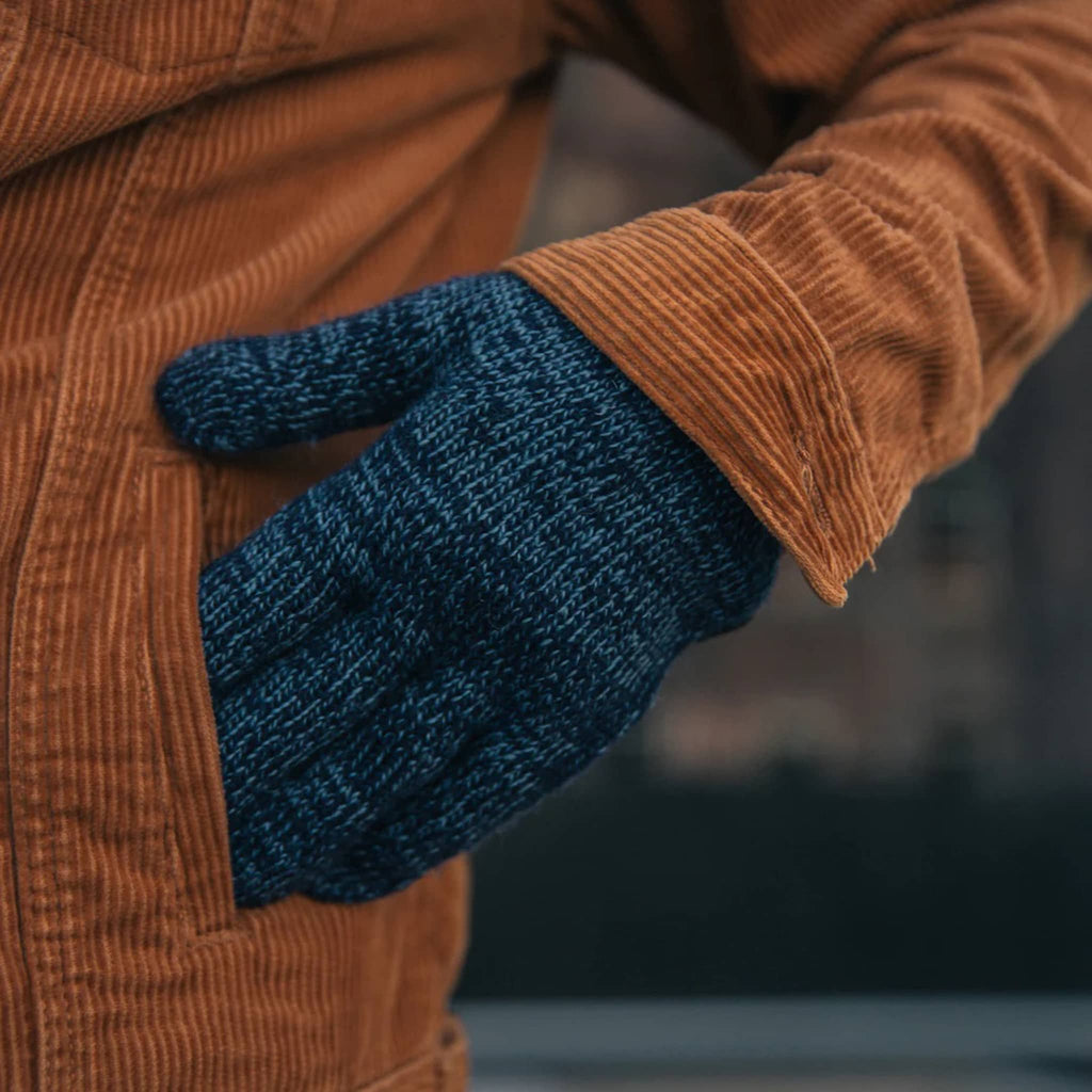 Blue knitted glove on a person wearing a brown jacket.