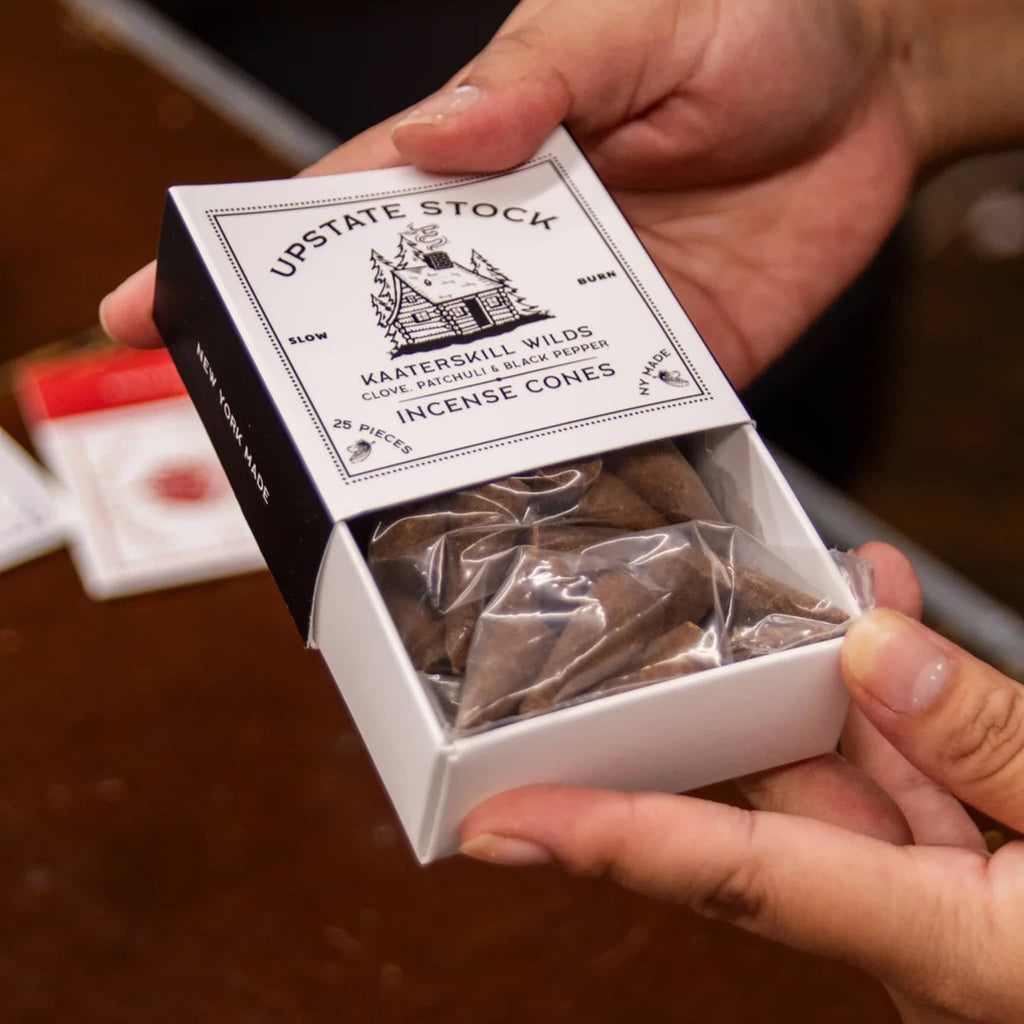 Box of Upstate Stock Incense Cones held by a person with a blurred background.