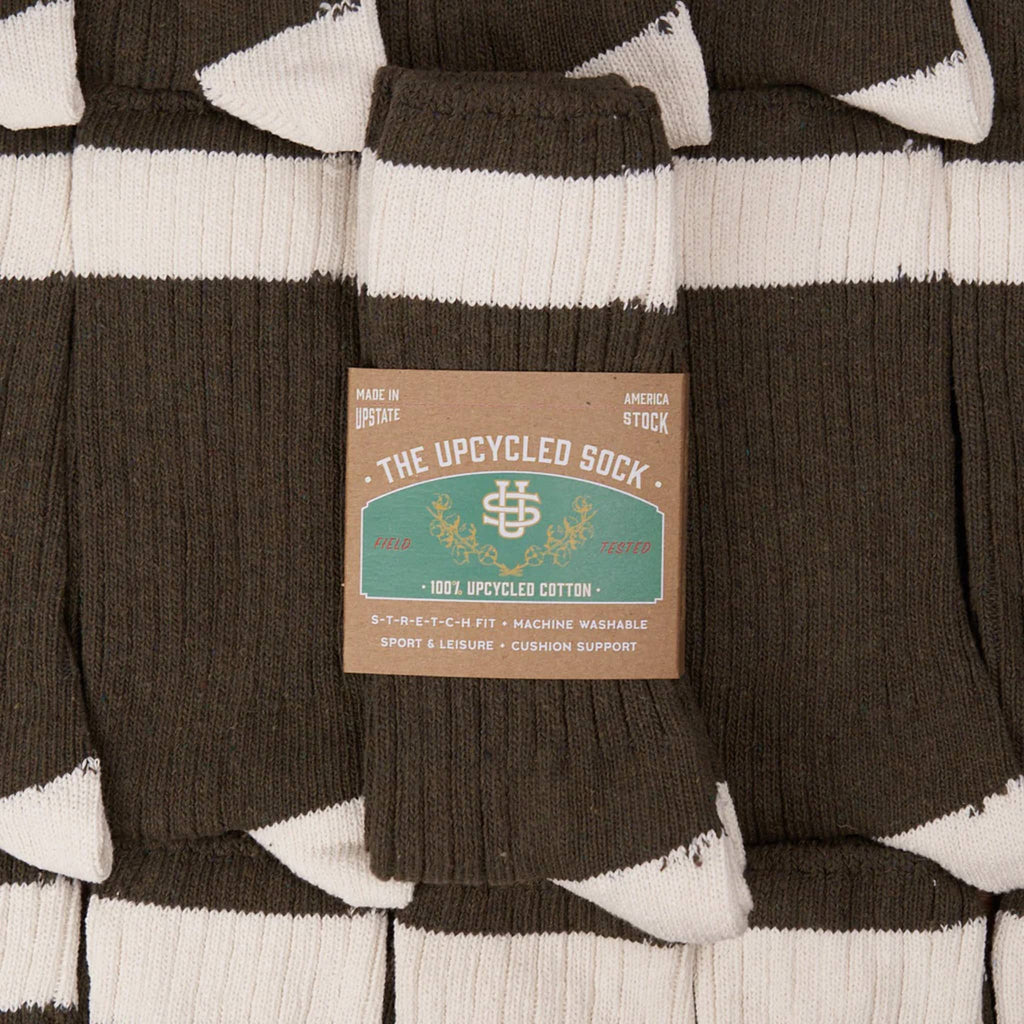 Pair of olive and white striped socks with a label on top, on a stack of the same socks without packaging.