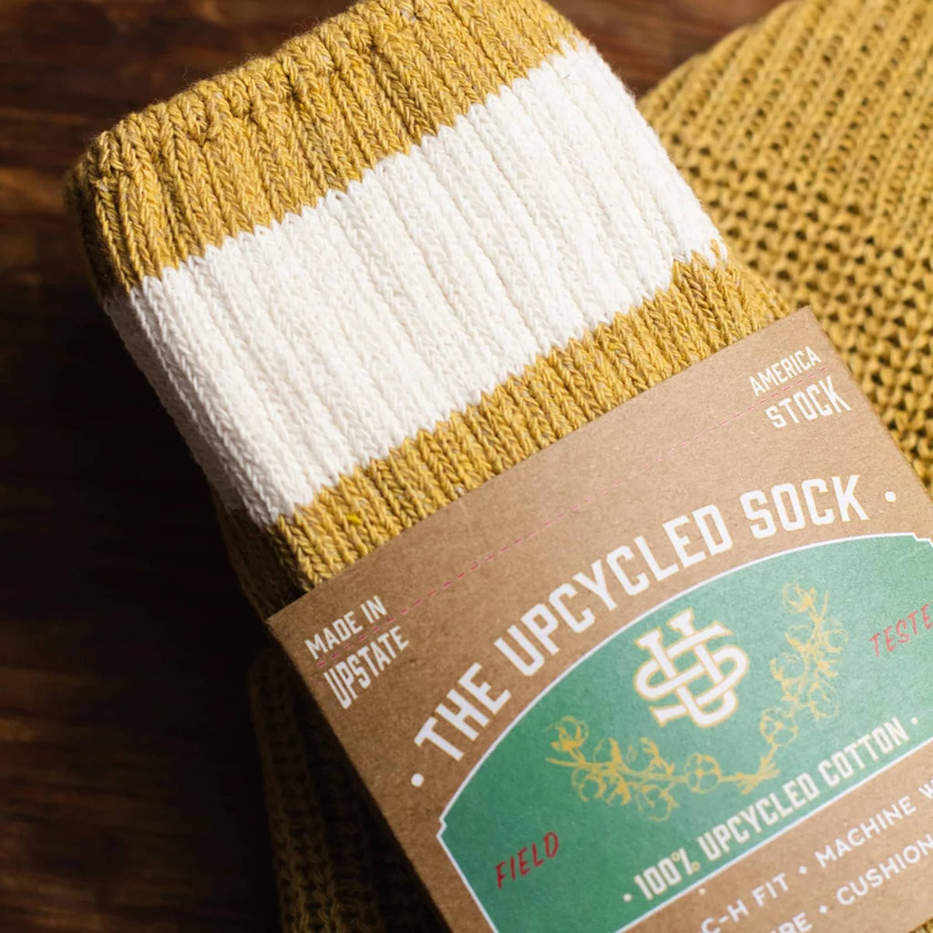 Detail of mustard yellow and white upcycled cotton sock with a packaging, on a wooden surface.