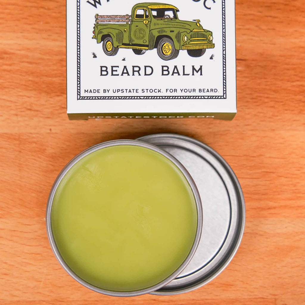 Beard balm in a metal container with a decorative box on a wooden surface.