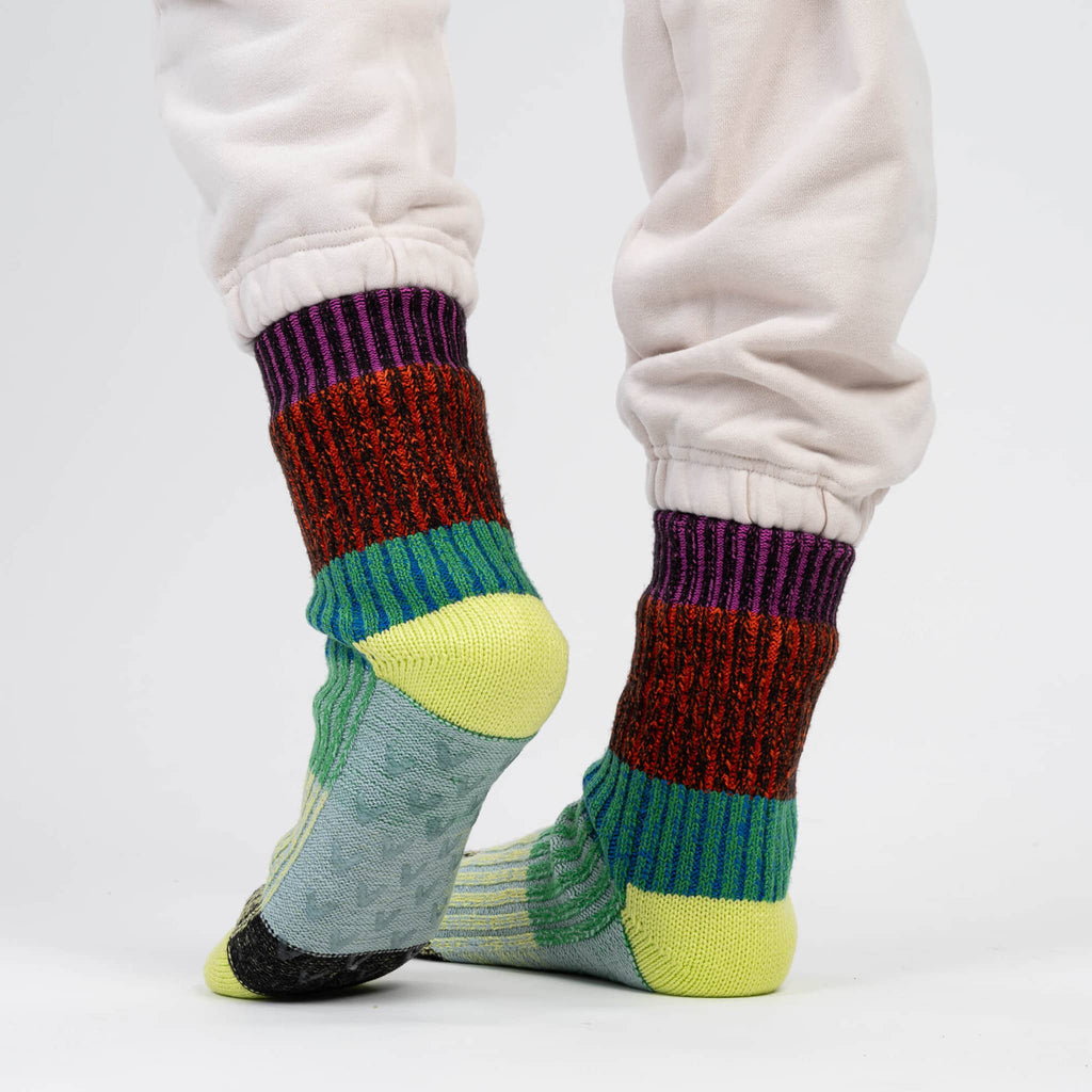 Verloop Mosaic Lime and Cobalt color-blocked house slipper socks worn with white sweatpants on a gray background.