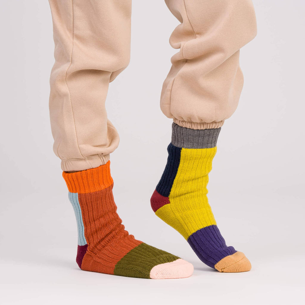 Verloop Mismatch Desert color-blocked house slipper socks worn with beige sweatpants on a gray background.