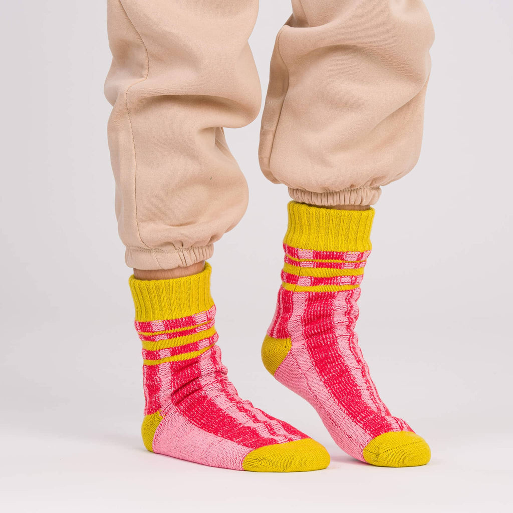 Verloop Plaid Stripe red, pink and yellow color-blocked house slipper socks worn with beige sweatpants on a gray background.