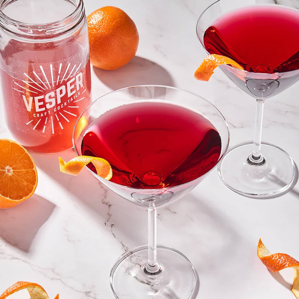 Vesper Cocktails Cosmpolitan Craft Cocktail Infusion Kit in mason jar with finished cocktails in coupe glasses with orange rind garnish.