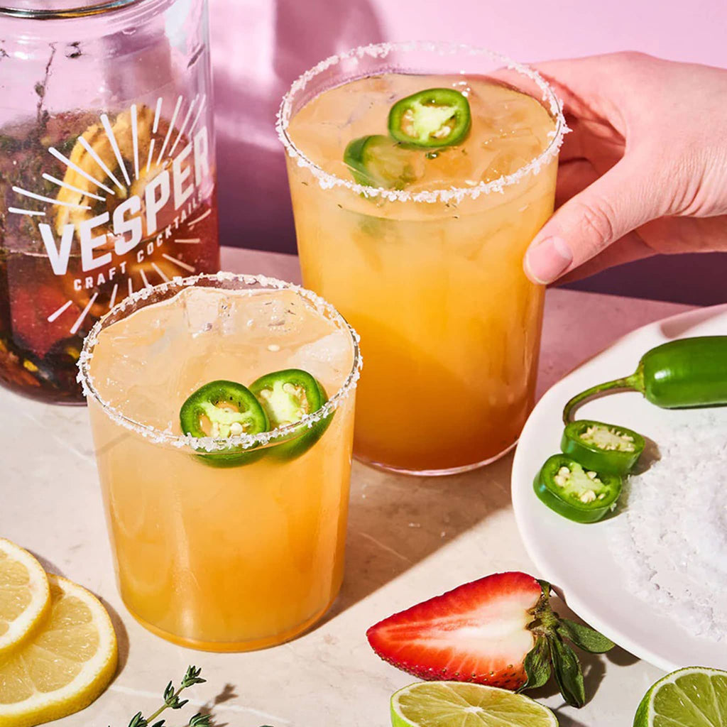 Vesper Jalapeno Margarita craft cocktail infusion kit shown with half empty jar and finished margaritas in glasses with salt rim and jalapeno slices to garnish.