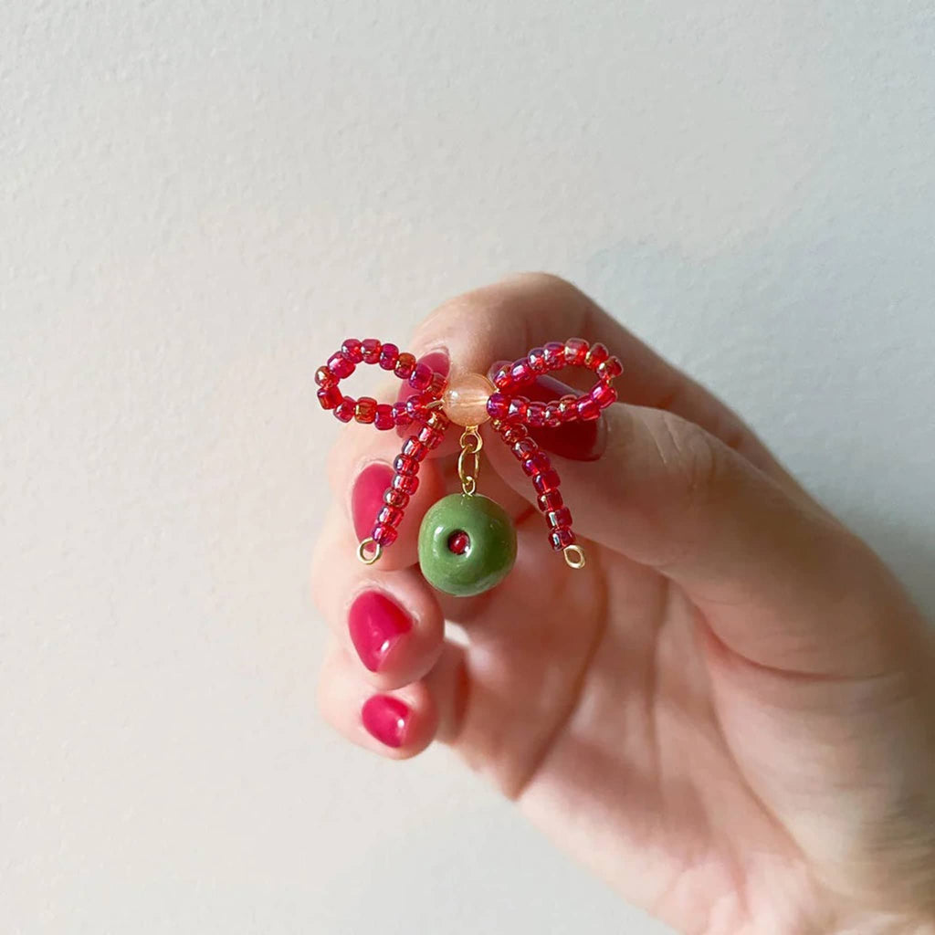 Hand holding a beaded pink bow earring with green olive made from clay, on a white background.