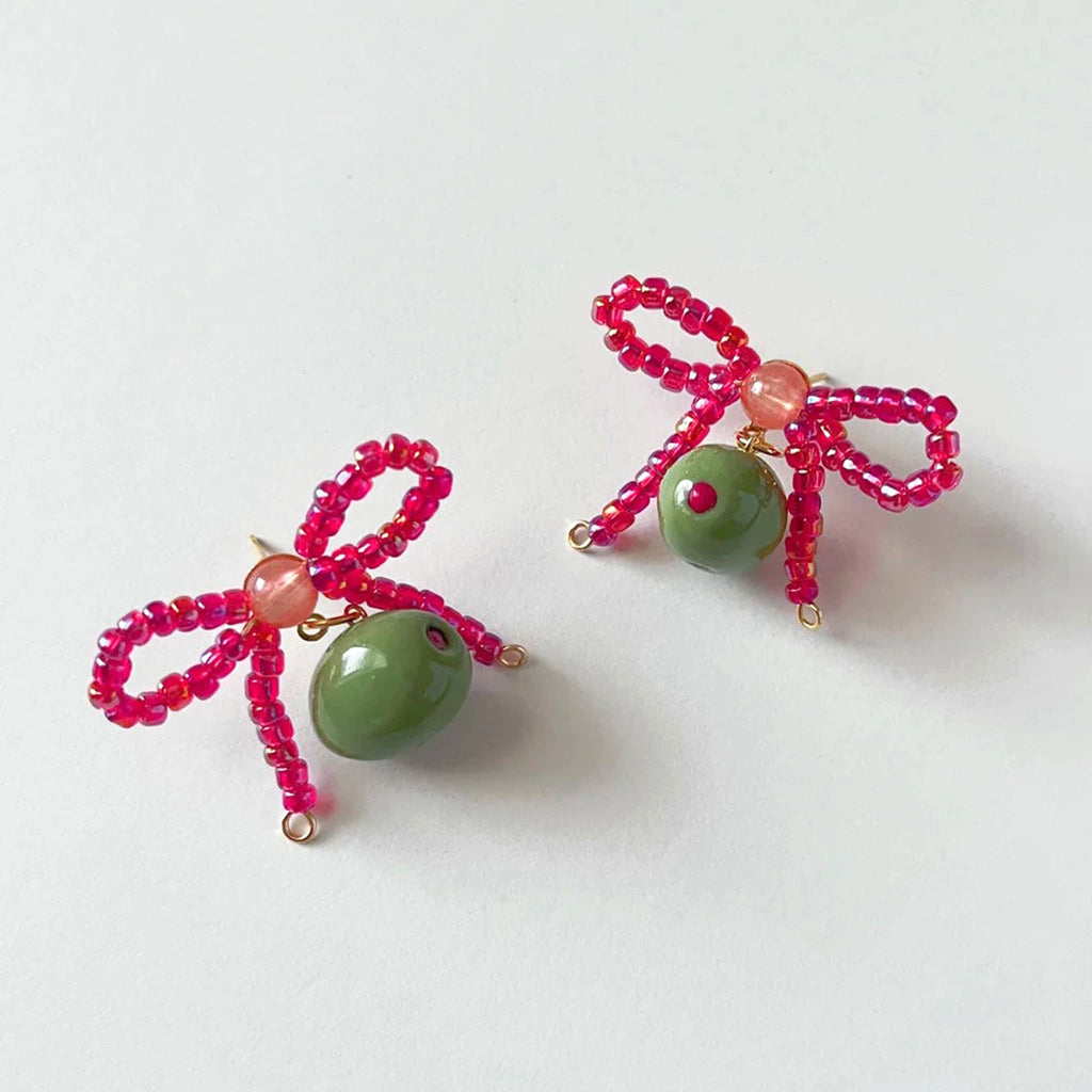 Beaded pink bow earrings with green olives made from clay, on a white background.