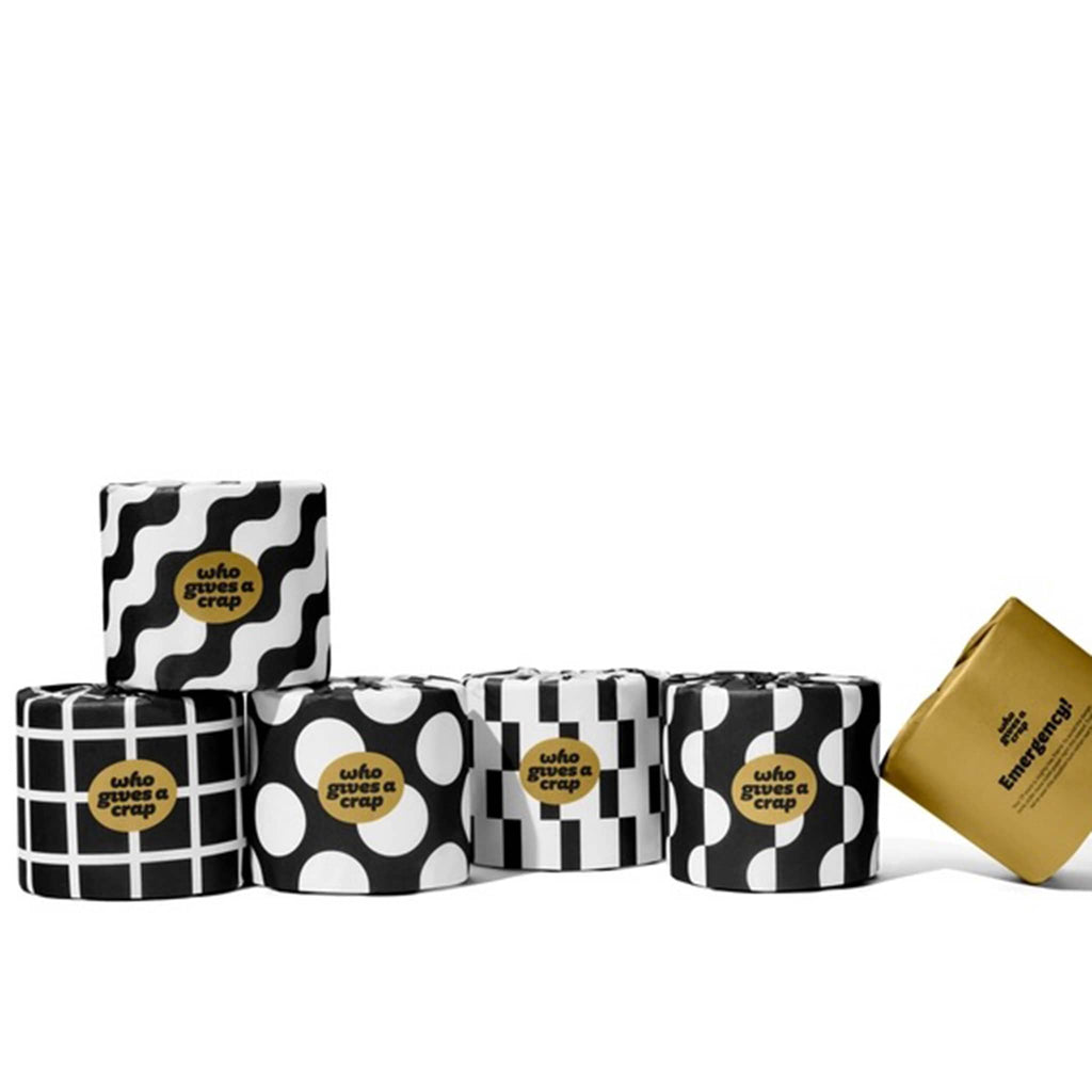 Who Gives a Crap Premium 100% Bamboo Toilet Paper Rolls wrapped in black and white paper with various designs and an "emergency" roll in gold.